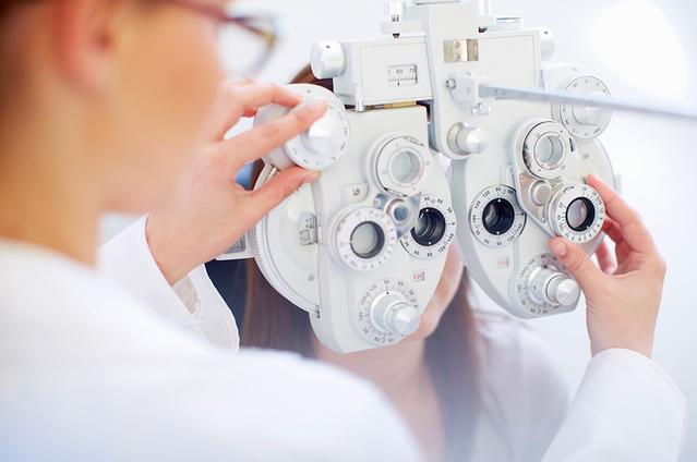 Une jeune femme derrière un phoroptère pendant que l’ophtalmologue lui vérifie ses yeux durant un examen oculaire.